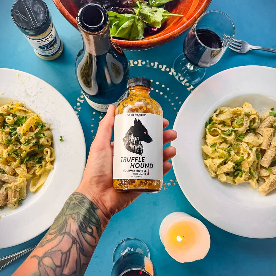 hand holding bottle of Truffle hound hot sauce above two plates of pasta