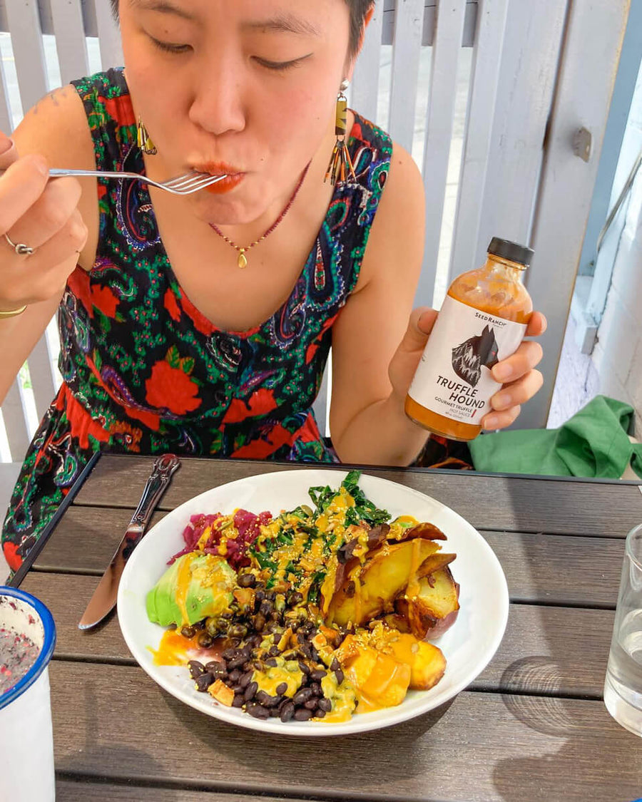 Woman eating a plate of vegan food drizzled with Truffle Hound hot sauce on top